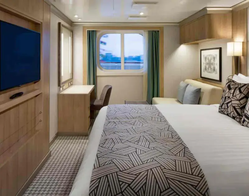 Ocean View stateroom with a large window, queen bed, and modern wooden furnishings aboard a Holland America cruise ship.
