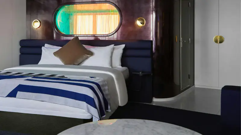 Virgin Voyages Gorgeous Suite bed beneath an oval shower window