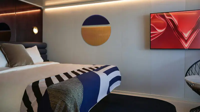 Virgin Voyages Sweet Aft Suite bed beside a television and red wall artwork