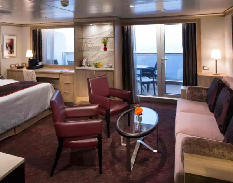 Neptune Suite with king bed, sitting area, glass coffee table, and private balcony view aboard a Holland America cruise ship.