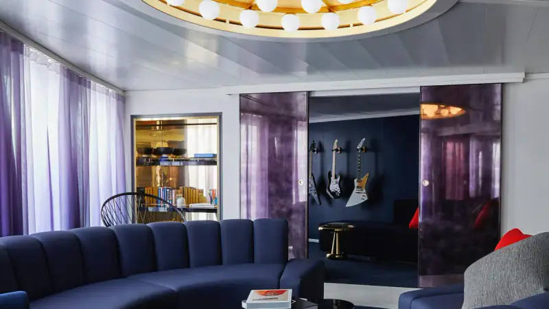 Virgin Voyages Massive Suite living area with a television and balcony windows