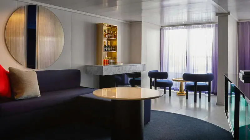Virgin Voyages Posh Suite living area with a sofa, desk, and windows