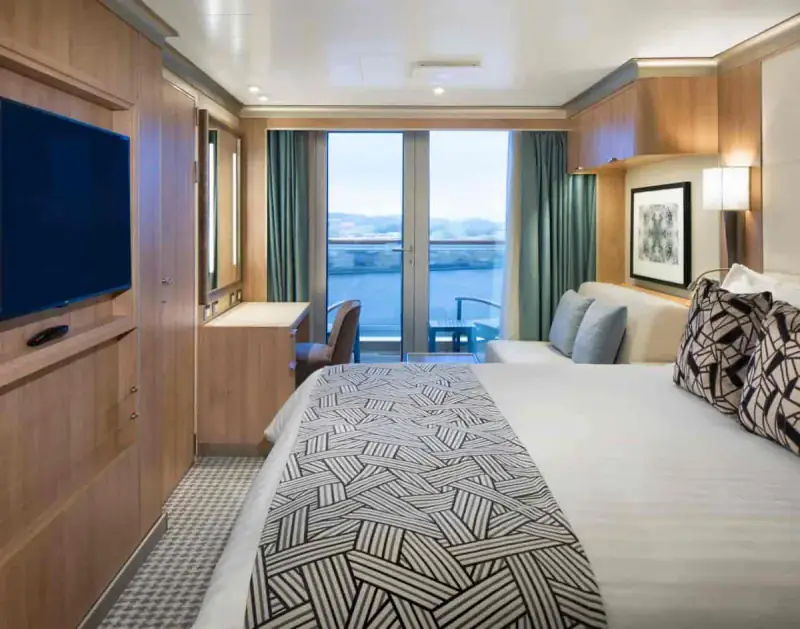 Verandah stateroom with queen bed, modern furnishings, and private balcony aboard a Holland America cruise ship.