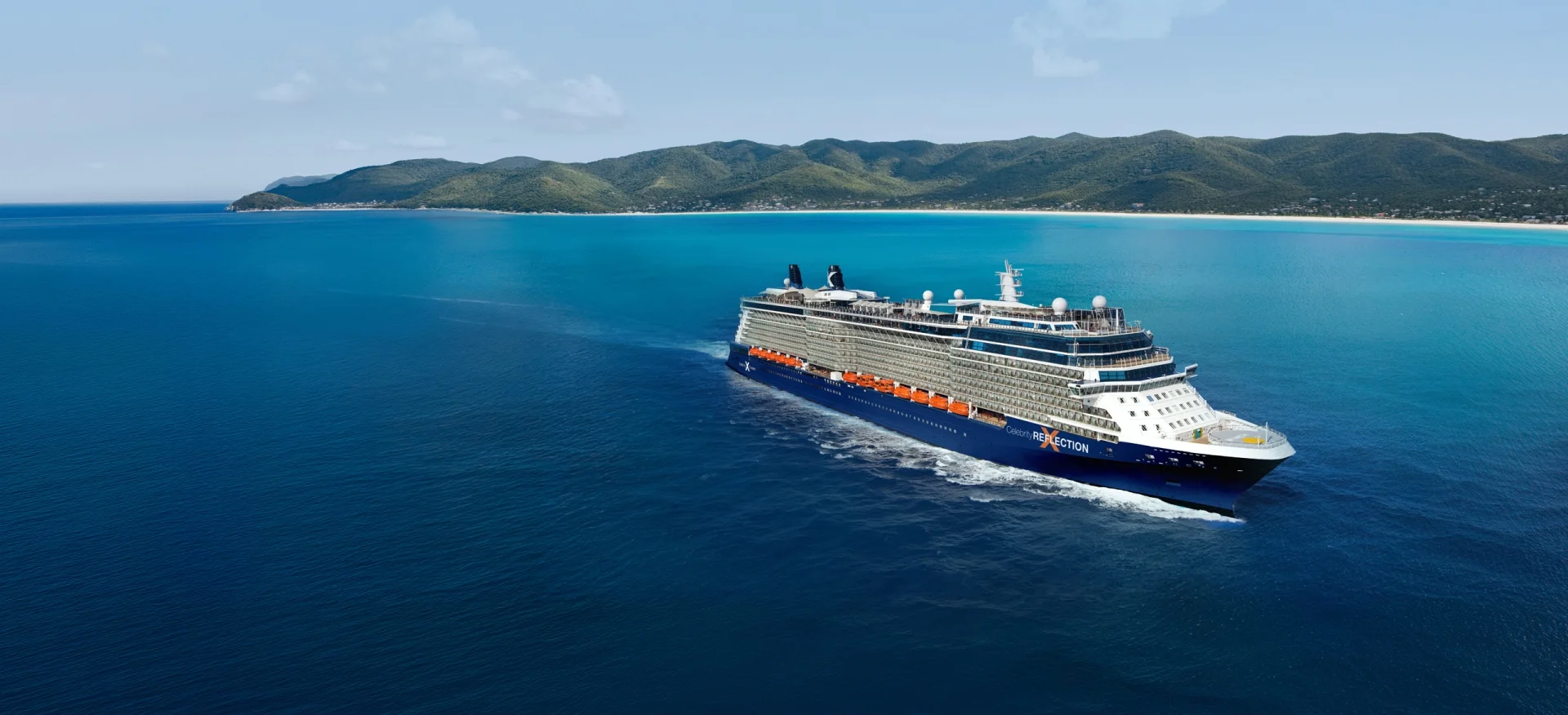 Celebrity Reflection sailing through blue Caribbean water with a green island beyond
