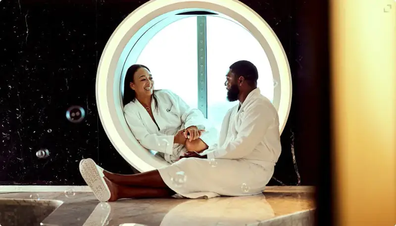 Two Sailors in robes relaxing beside a round window in Scarlet Lady's spa