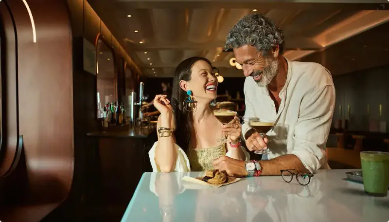 Sailor holding a cocktail at a colorful bar aboard Valiant Lady