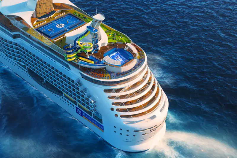 A Royal Caribbean cruise ship is photographed from above in blue water.