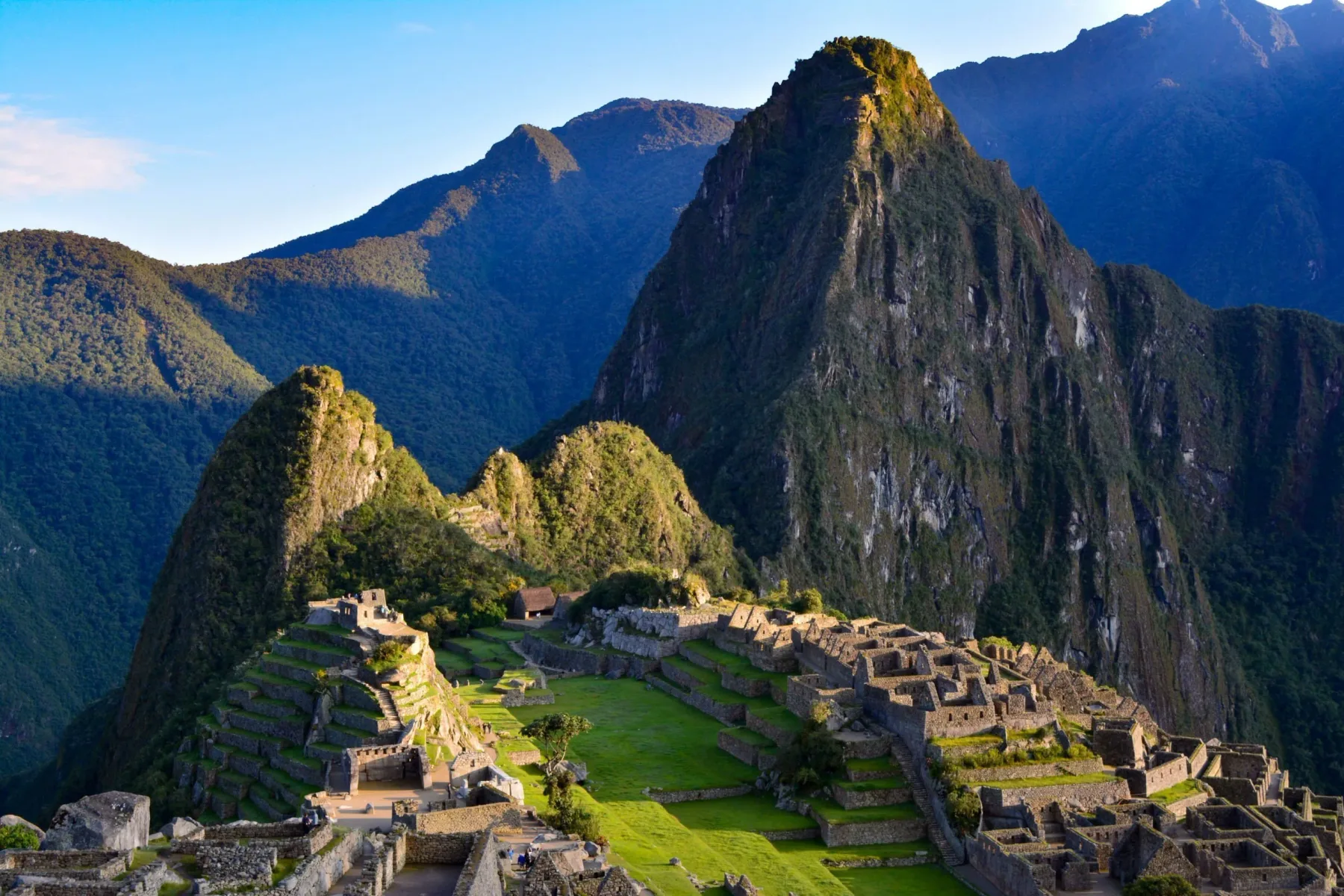 Machu Picchu rises above a green mountain ridge under a blue sky.