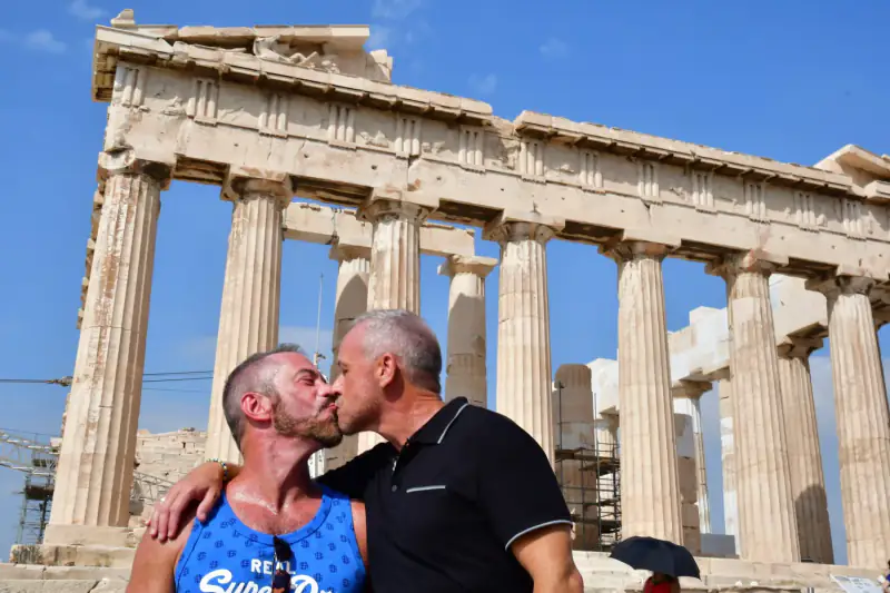 Two men kiss beside the Parthenon in Athens.