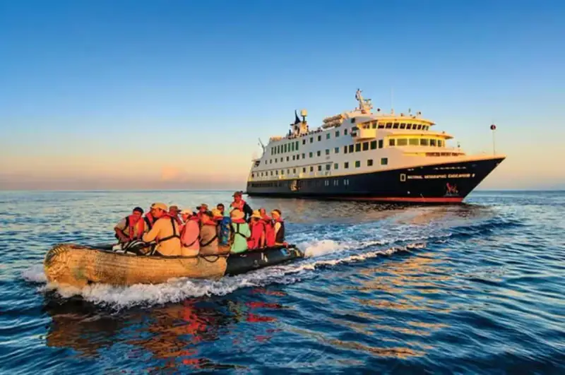 National Geographic Endeavour II sails at sea beside an inflatable Zodiac.