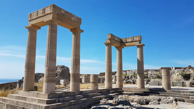 Ancient stone columns stand against a blue sky in the Greek Isles.