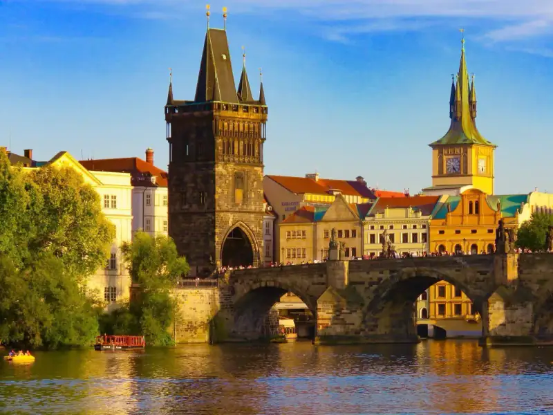A historic Prague skyline and riverside buildings glow in evening light.