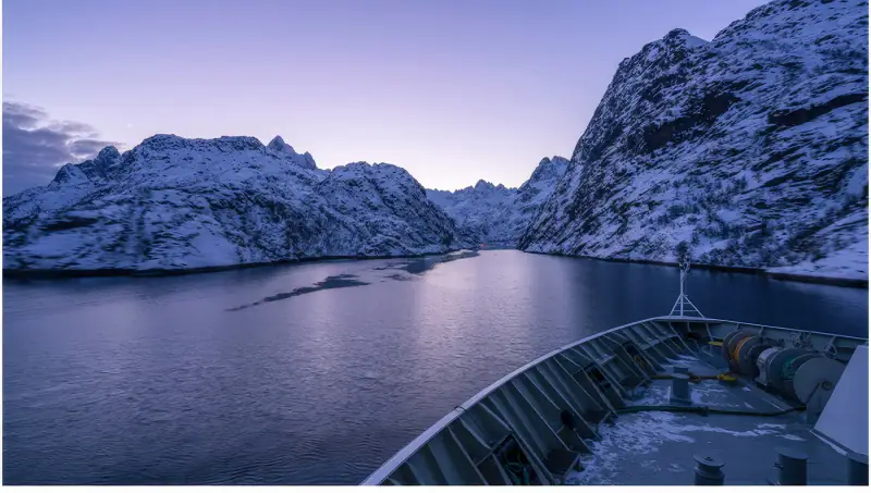 A fjord winds between snow-covered mountains beneath a pale sky.