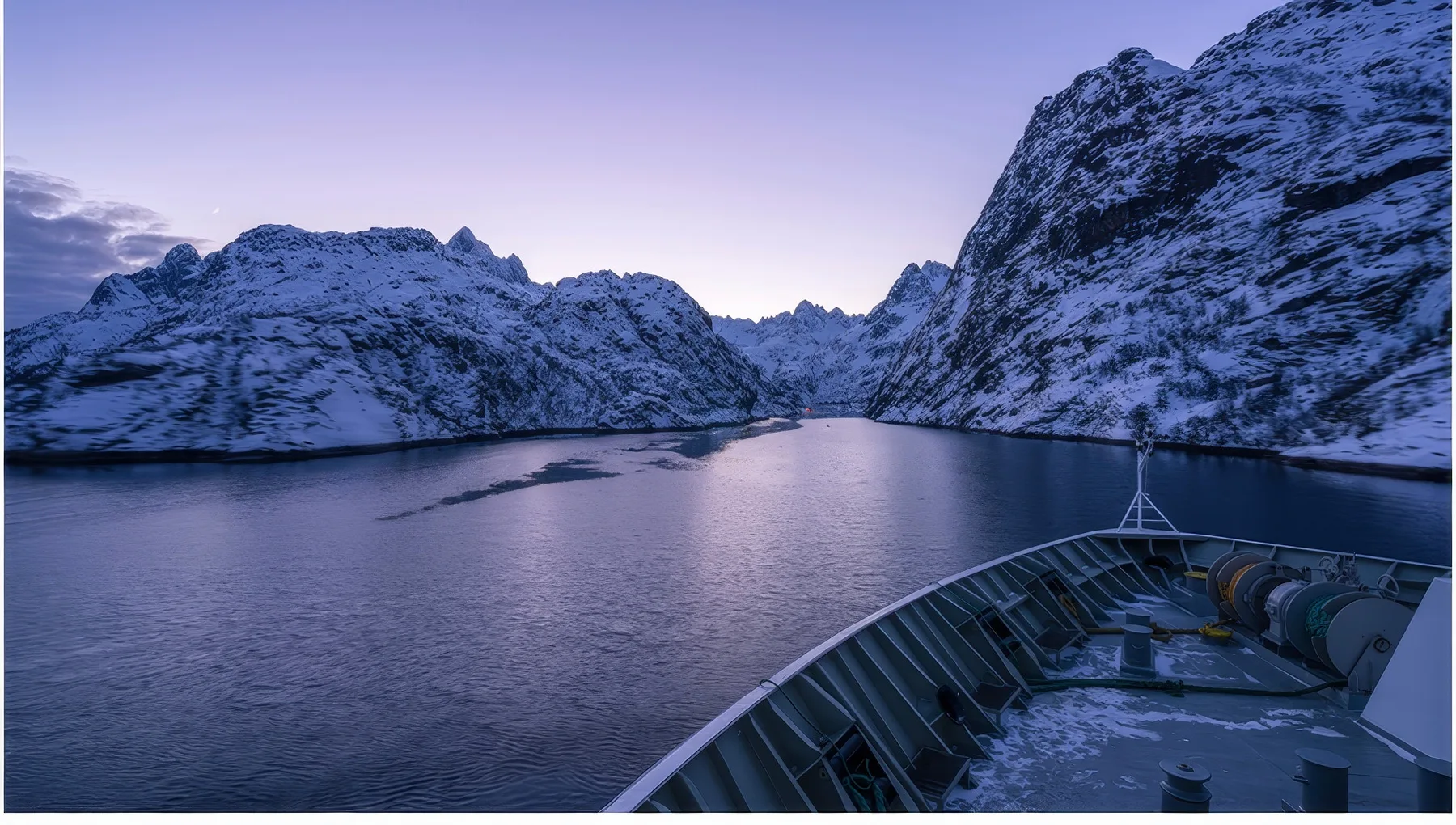A fjord winds between snow-covered mountains beneath a pale sky.