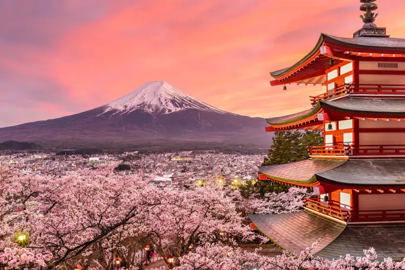 Mount Fuji rises behind a red pagoda and autumn-colored trees.