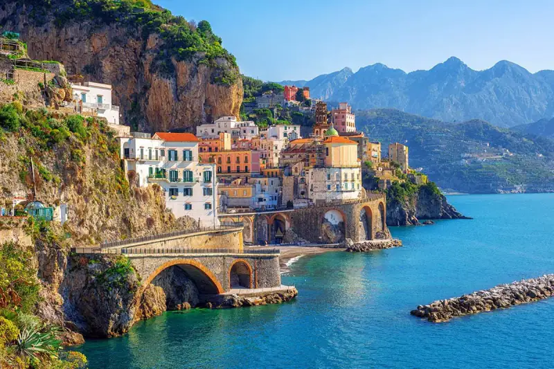 A sunlit Mediterranean cliffside town overlooks deep blue water.