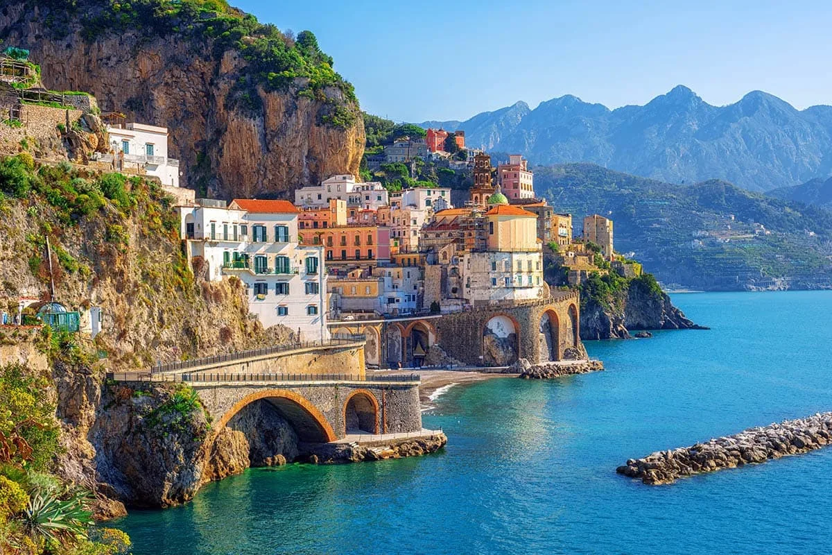 A sunlit Mediterranean cliffside town overlooks deep blue water.