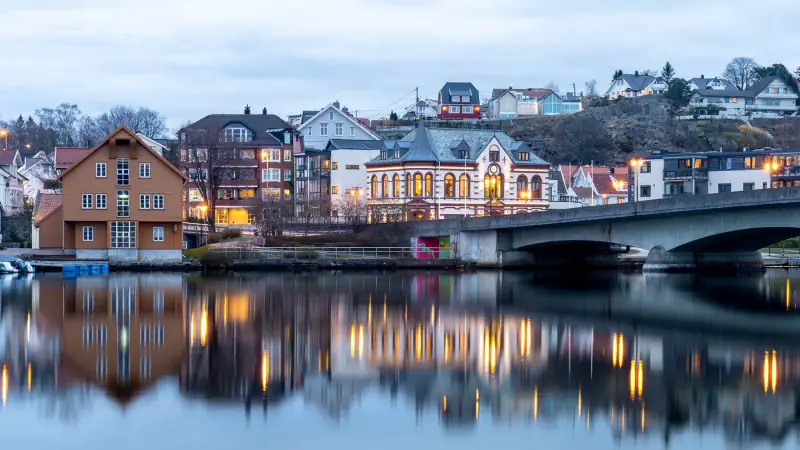 A quiet waterfront town sits below a mountain and a cloudy northern sky.