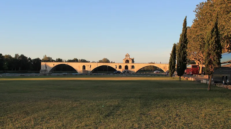 Stone arches of Pont Saint-Bénézet in Avignon at sunset, seen from a grassy riverbank