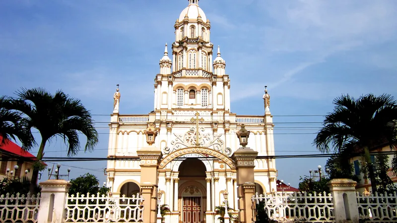Pale yellow façade and central tower of Cù Lao Giêng church between palm trees on the island