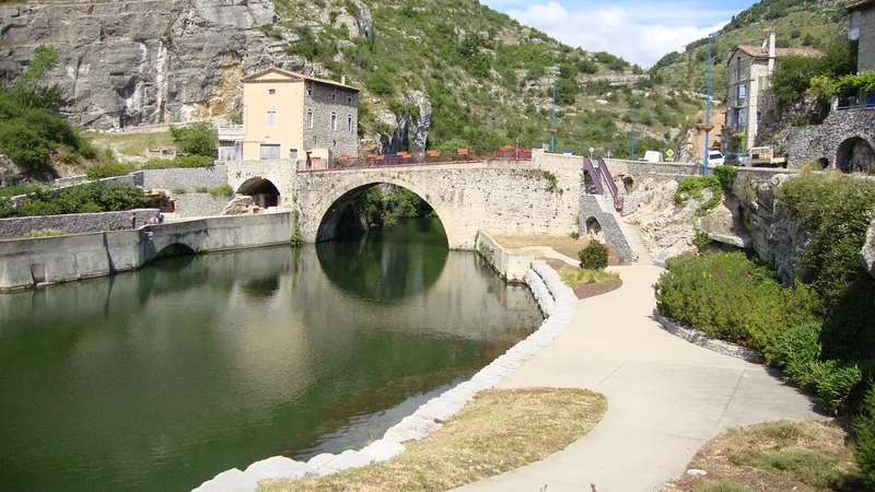 Single-arched Roman bridge over the Ouvèze in Le Pouzin, with riverside paths, houses and rocky hills