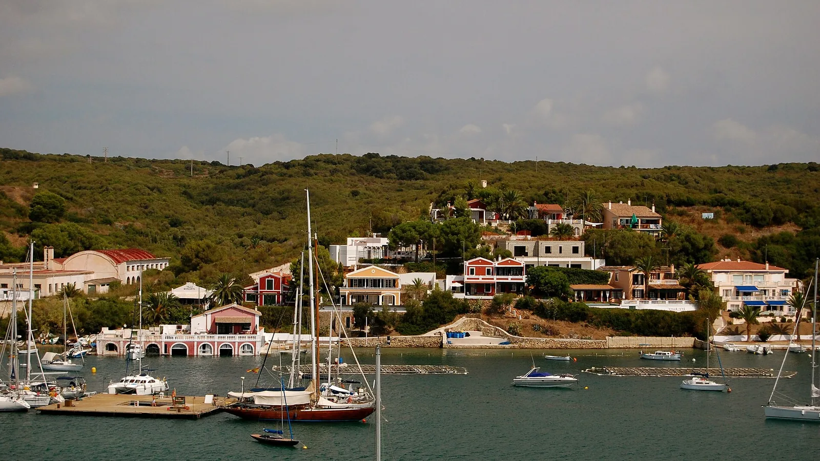 Sailboats and colorful waterfront homes around Mahón's natural harbor