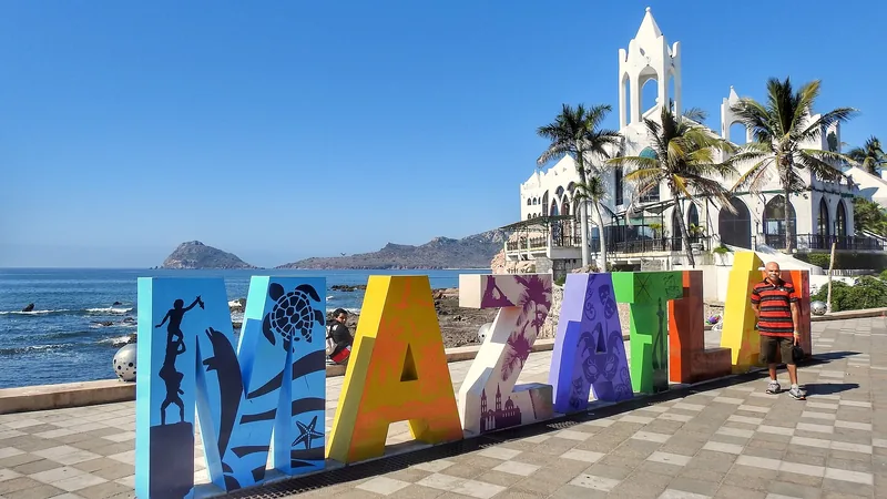 Colorful Mazatlán sign on the waterfront with palms and a church