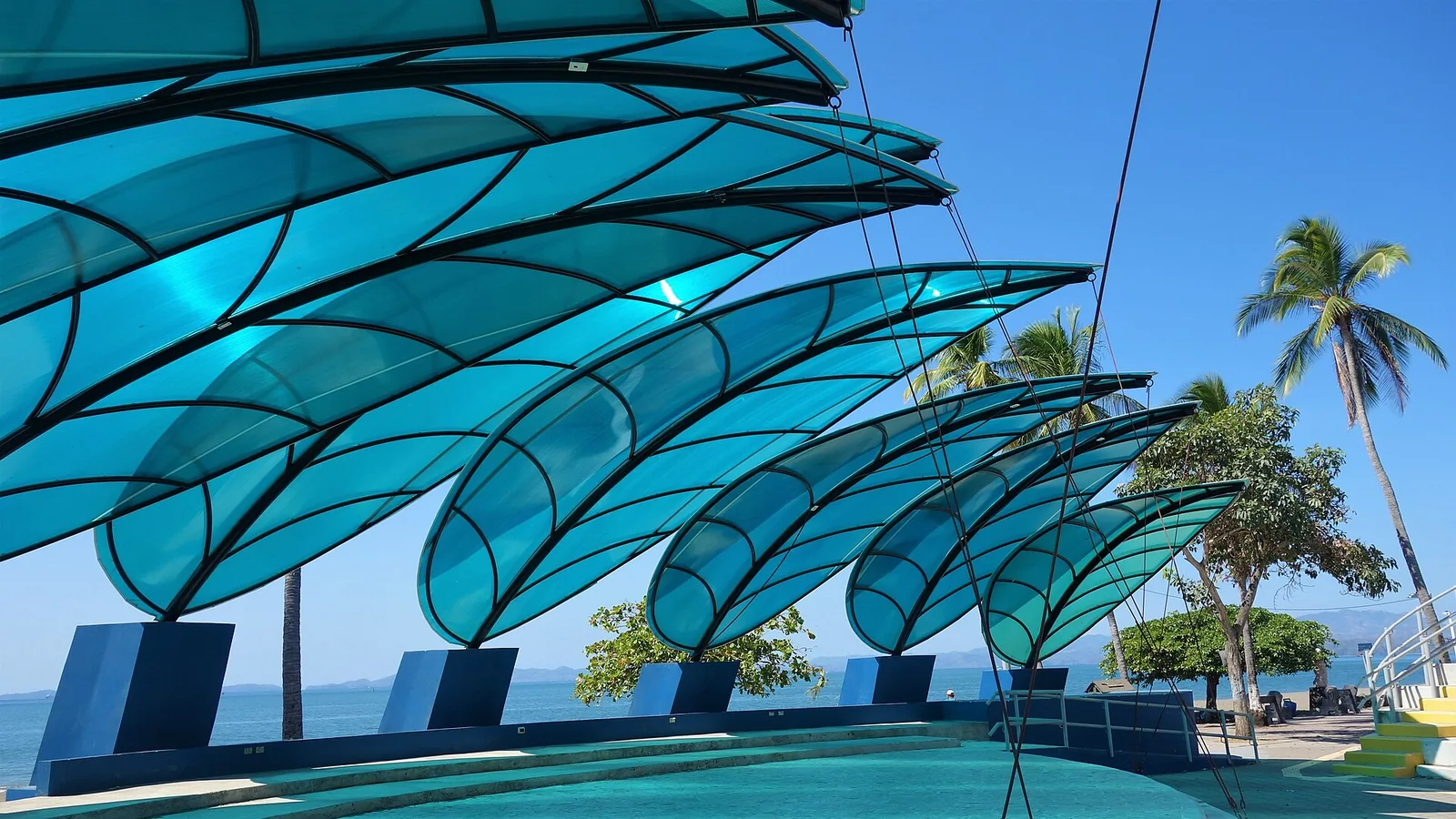 Blue wave-shaped shade canopies, palm trees, and the Puntarenas waterfront
