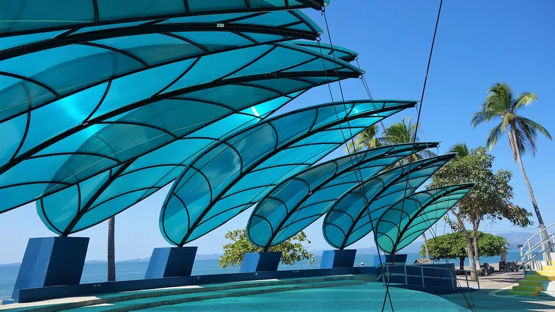 Blue wave-shaped shade canopies, palm trees, and the Puntarenas waterfront