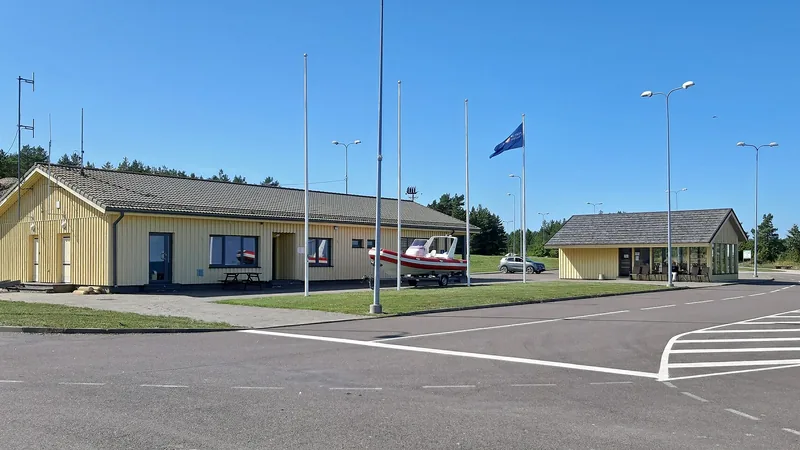Yellow harbor buildings, paved passenger area and woodland at Saaremaa harbor in Ninase; a historical photograph